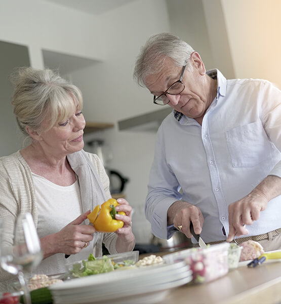 um casal de idosos está an cozinha cortando alguns legumes