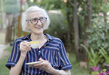 uma senhora sorri e toma um chá em um jardim