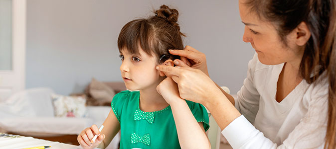 mãe ajuda filha a inserir o aparelho auditivo