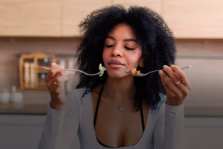 Ao fundo imagem de uma mulher olhando para dois talheres com alimentos