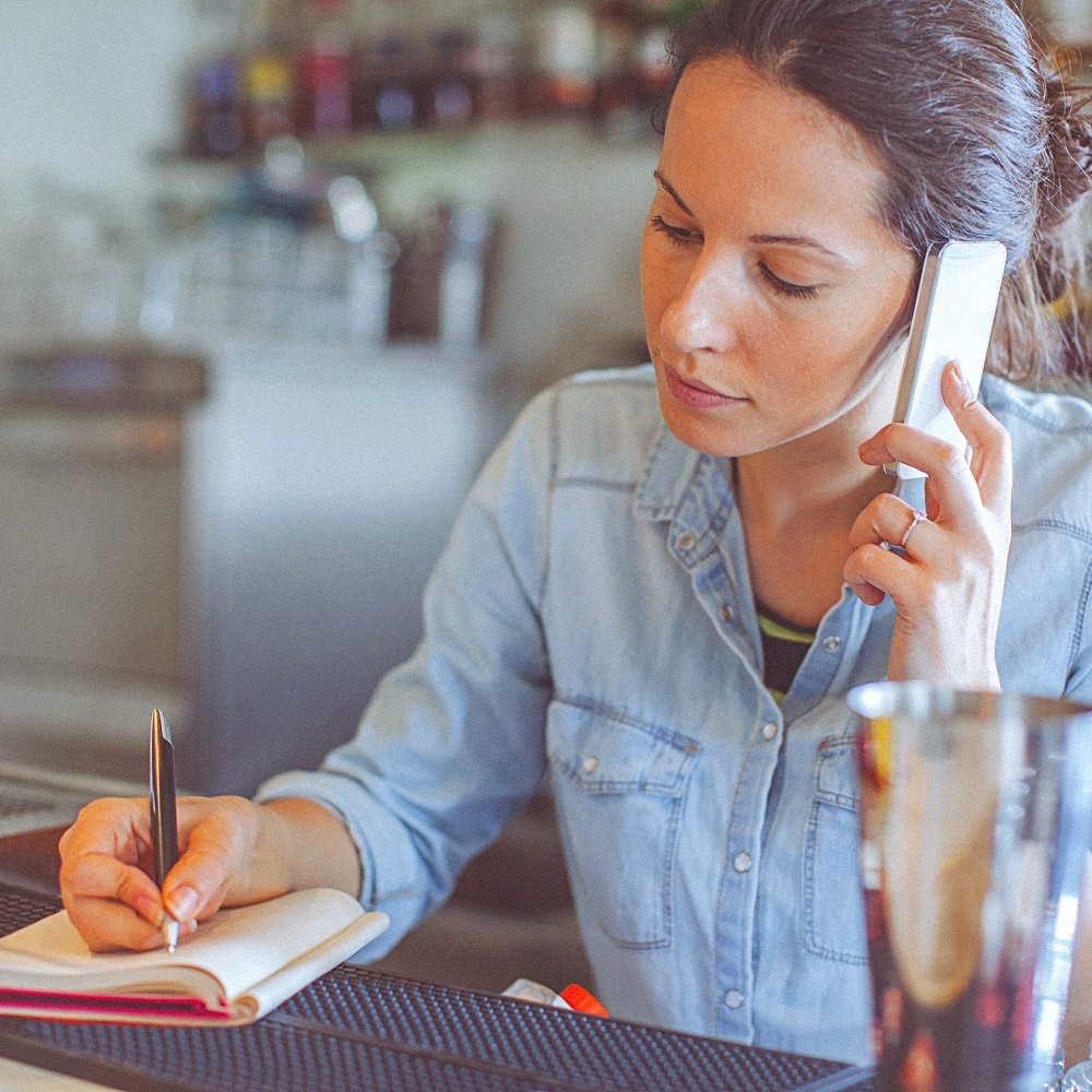Mulher ao telefone, anotando informações em um caderno.